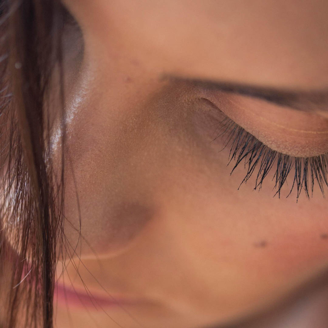 Nahaufnahme des Gesichts einer Person mit Fokus auf die Augenpartie. Die Wimpern sind lang und dunkel, ein Auge ist teilweise geschlossen. Weiches Licht hebt die Haut und die feinen Gesichtszüge hervor und schafft eine intime und heitere Atmosphäre. Ein paar Haarsträhnen sind sichtbar. Nahaufnahme des Gesichts einer Person mit Fokus auf die Augenpartie. Die Wimpern sind lang und dunkel, ein Auge ist teilweise geschlossen. Weiches Licht hebt die Haut und die feinen Gesichtszüge hervor und schafft eine intime und heitere Atmosphäre. Ein paar Haarsträhnen sind sichtbar.