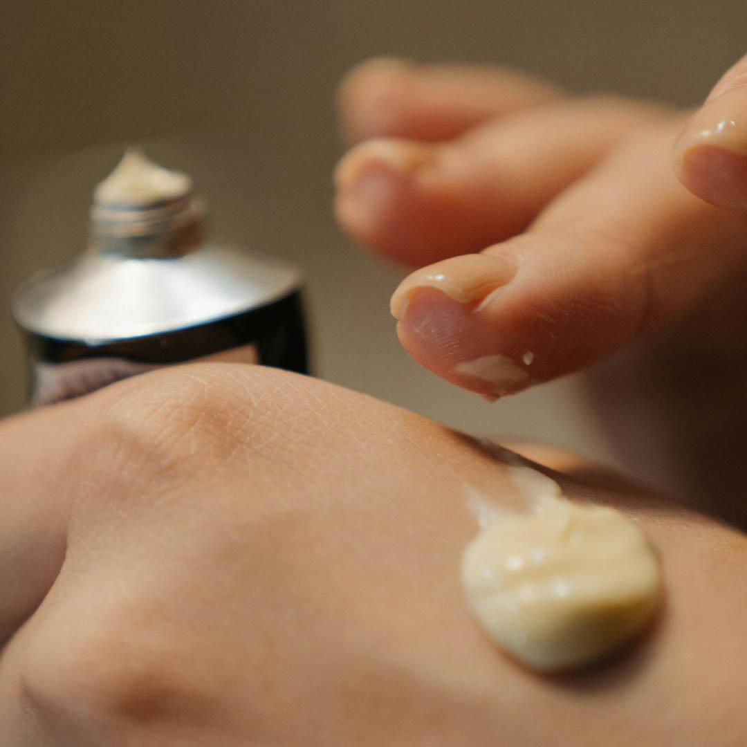 Eine Hand mit einem kleinen Klecks Creme wird aus einer Metalltube gedrückt. Ein anderer Finger berührt die Creme, was darauf schließen lässt, dass das Produkt auf die Haut aufgetragen oder verteilt wird. Der Hintergrund ist unscharf. Eine Hand mit einem kleinen Klecks Creme wird aus einer Metalltube gedrückt. Ein anderer Finger berührt die Creme, was darauf schließen lässt, dass das Produkt auf die Haut aufgetragen oder verteilt wird. Der Hintergrund ist unscharf.