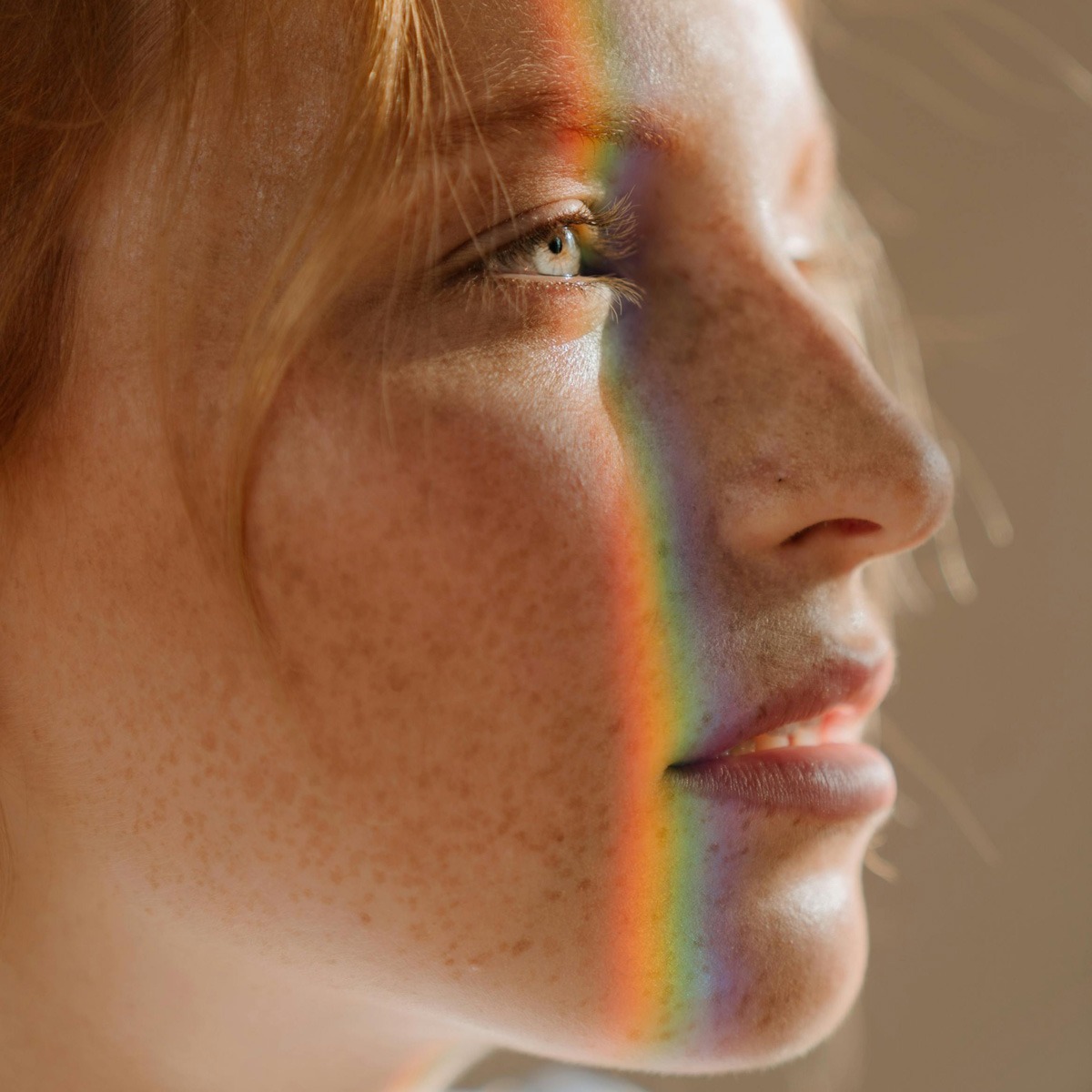 Eine Nahaufnahme des Profils einer Person mit Sommersprossen, teilweise beleuchtet durch einen Regenbogen, der ihr Gesicht überzieht. Der Blick der Person ist nach oben gerichtet und das warme Licht betont die Details ihrer Haut und Haare. Eine Nahaufnahme des Profils einer Person mit Sommersprossen, teilweise beleuchtet durch einen Regenbogen, der ihr Gesicht überzieht. Der Blick der Person ist nach oben gerichtet und das warme Licht betont die Details ihrer Haut und Haare.